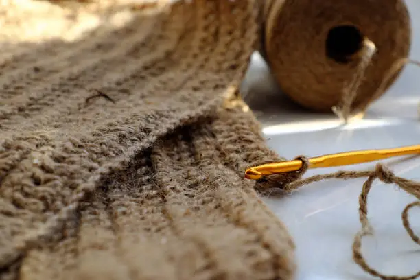 Close up crochet hook with ball of jute rope to make decor handmade product, table dishcloth or mat on white background