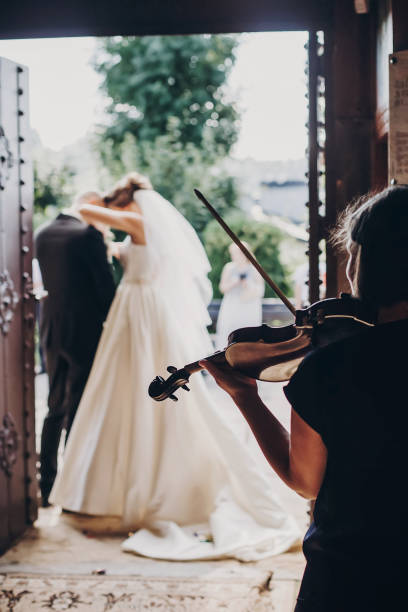 músico tocando el violín mientras que hermosos novios de pie en la iglesia después del matrimonio de la boda. elegante cuarteto de cuerda actuando en la ceremonia de la boda, toque de primer plano de la orquesta - violin family fotografías e imágenes de stock