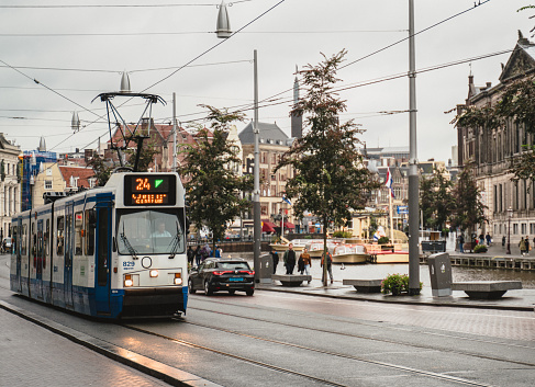 Amsterdam, The Netherlands - October 11, 2019: Red tram is going  with passengers near canal in Amsterdam.People are walking in a hurry.
