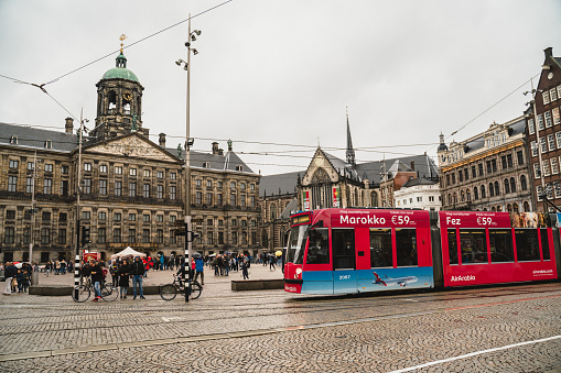 Amsterdam, The Netherlands - October 11, 2019: Red tram is waiting for passengers in Dam Square in Amsterdam.People are walking in a hurry.