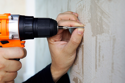 Screwing a screw into the wall with an electric screwdriver close-up. Repair in the apartment or house.