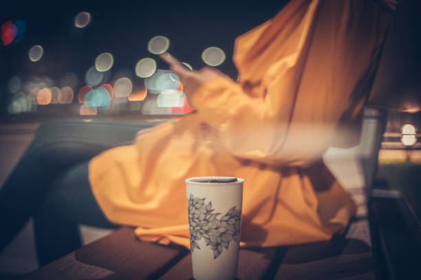 A woman in a yellow coat relaxing on a bench while her reusable, portable porcelain coffee cup rests next to her.