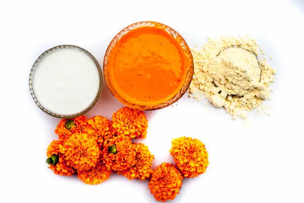 Marigold flower face mask consisting of some besan or chickpea flour well mixed with milk in a glass bowl isolated on white along with marigold flowers and some flour.Horizontal top shot.
