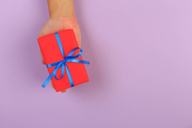 istock gift in female hands on a colored background top view. 1182810527
