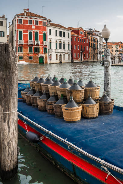 Boat moored to the shore of the Grand Canal in Venice with empty wine vessels.