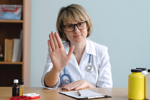 Woman a doctor is showing a stop gesture by her hand. No panic. Do not worry concept. Denial in medical examination.