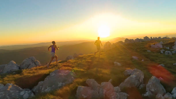 istock AERIAL, LENS FLARE: Athletic young couple jogging along a scenic grassy trail. 1182817192