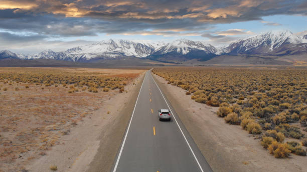 aerial: gran suv conduce por la carretera vacía que conduce a las espectaculares montañas rocosas. - autopista fotos fotografías e imágenes de stock
