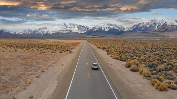 AERIAL: Large SUV drives down empty highway leading to the spectacular Rockies.
