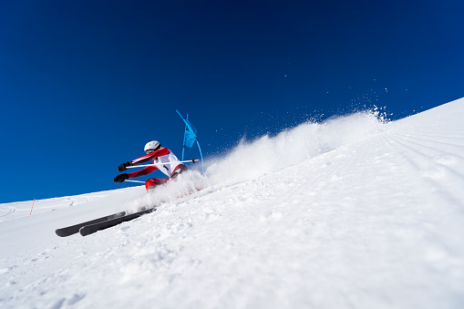 wide angle view low perspective dynamic aggressive focused professional ski racer skiing giant slalom on sunny winter day with clear blue sky snow slpashing