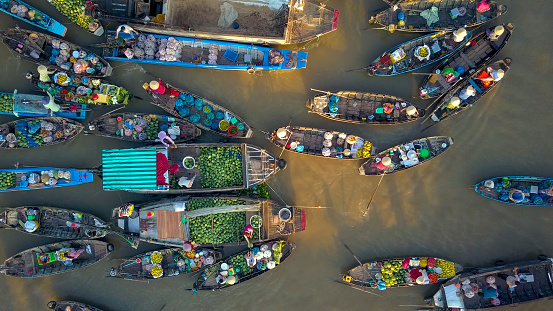 AERIAL, TOP DOWN: Local people buying and selling colorful produce from traditional wooden boats floating around the murky delta in the scenic Asian countryside on an idyllic sunny summer evening.