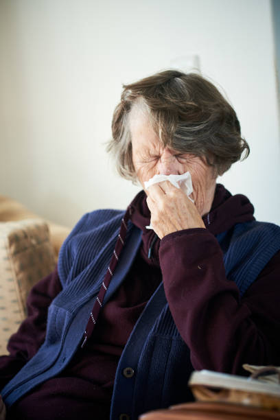 istock Senior woman sitting on sofa sneezing unhappily 1182820632