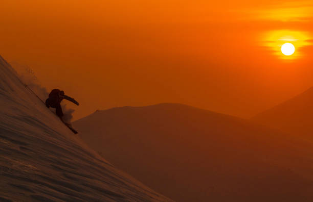 sylwetka: pomarańczowe poranne słońce oświetla narciarzy freeride rozdrabniających śnieg w proszku. - skiing winter sport powder snow athlete zdjęcia i obrazy z banku zdjęć