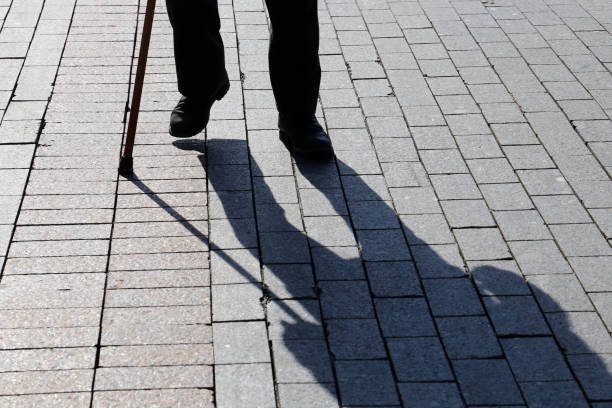istock Shadow and silhouette of limping man walking with a cane on pavement 1182821864