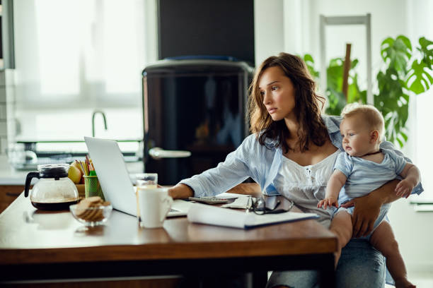 istock Young mother working on laptop while being with baby at home. 1182821936