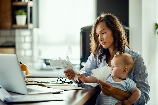 Young mother with baby going through bills while analyzing her home finances.