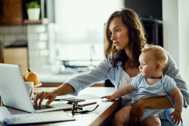 istock Working mother using laptop while being with baby at home. 1182823576