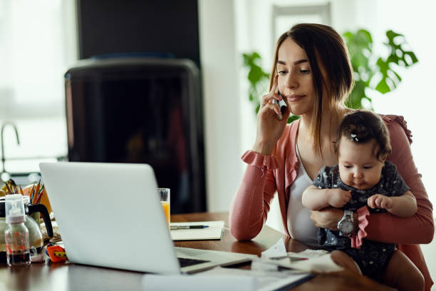 istock Young mother talking on the phone while using laptop at home. 1182824513