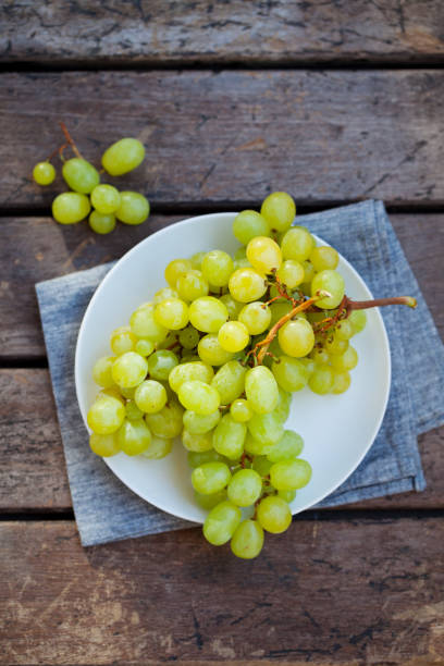 Green grape on a white plate. Grey wooden background. Top view. Copy space