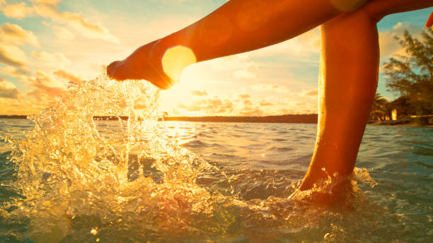 istock LENS FLARE: Unrecognizable woman having fun kicking the refreshing ocean water. 1182825704