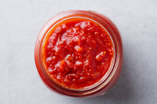 Tomato sauce in a glass jar. Grey background. Close up. Top view.