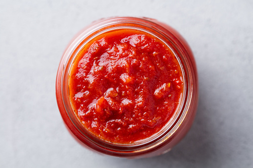 Tomato sauce in a glass jar. Grey background. Close up. Top view