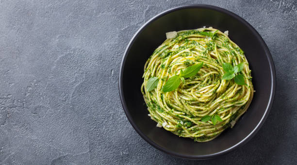 Pasta spaghetti with pesto sauce and fresh basil leaves in black bowl. Grey background. Copy space. Top view. Pasta spaghetti with pesto sauce and fresh basil leaves in black bowl. Grey background. Copy space. Top view pesto sauce stock pictures, royalty-free photos & images