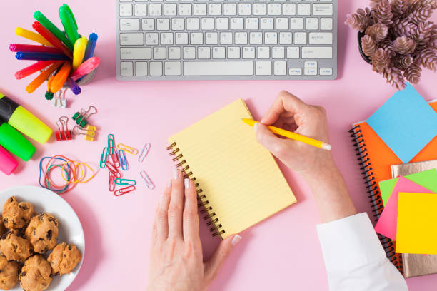 Woman working on office table. Top view pink trendy office table.