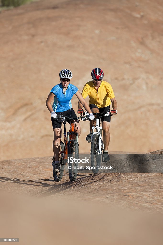 Pareja joven ciclismo de montaña en Petrified Dunas de arena - Foto de stock de Accesorio de cabeza libre de derechos