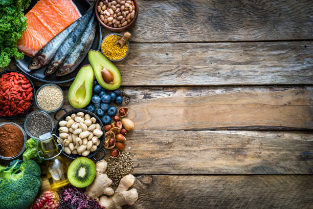 Healthy eating: selection of antioxidant group of food frame. Copy space Top view of healthy, antioxidant group of food placed at the left border of a wooden table leaving useful copy space for text and/or logo at the center right. The composition includes food rich in antioxidants considered as a super-food like avocado, kale, blueberries, chia seeds, broccoli, different nuts, salmon, sardines, pollen, quinoa, hemp seeds, seaweed, cocoa, olive oil, goji berries, kiwi fruit, pistachio, seaweed, pinto beans, pomegranate and ginger. XXXL 42Mp studio photo taken with SONY A7rII and Zeiss Batis 40mm F2.0 CF antioxidant stock pictures, royalty-free photos & images