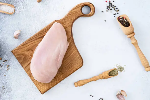 Photo of Top view of raw chicken meat on a black slate on the table. Raw chicken breast on a gray background