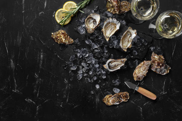 fresh opened oysters, ice, lemon on a rectangle slate and champagne are on a black stone textured background. top view with copy space. close-up - drink on top of ice food imagens e fotografias de stock