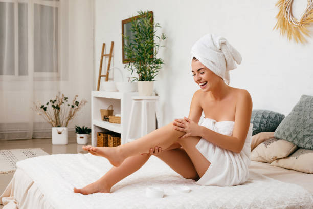 woman applying cream on her legs - moisturizer women cosmetics body imagens e fotografias de stock