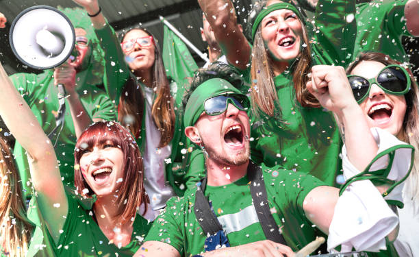 young amateur football fan supporters cheering with confetti watching local soccer cup match at stadium - friends people group on green t shirts having excited fun on sport world championship final - sport crowd fan stadium imagens e fotografias de stock