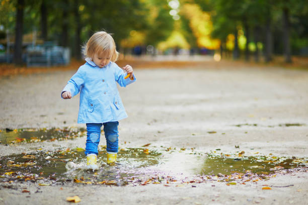 istock Child wearing yellow rain boots and jumping in puddle 1182846864
