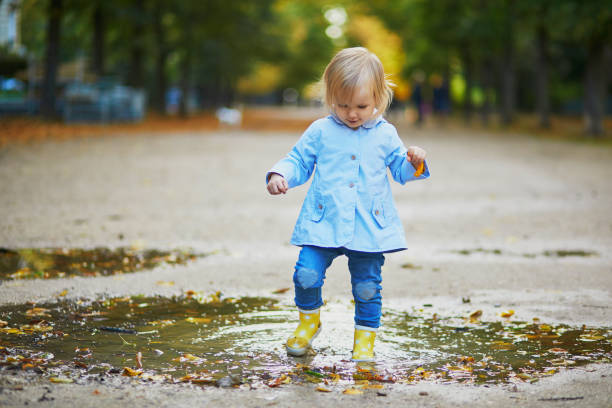 istock Child wearing yellow rain boots and jumping in puddle 1182846867