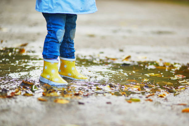 istock Child wearing yellow rain boots and jumping in puddle 1182846883