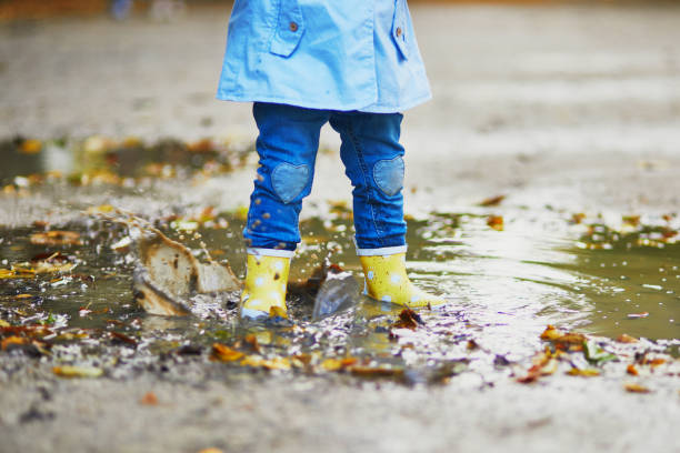 istock Child wearing yellow rain boots and jumping in puddle 1182846891