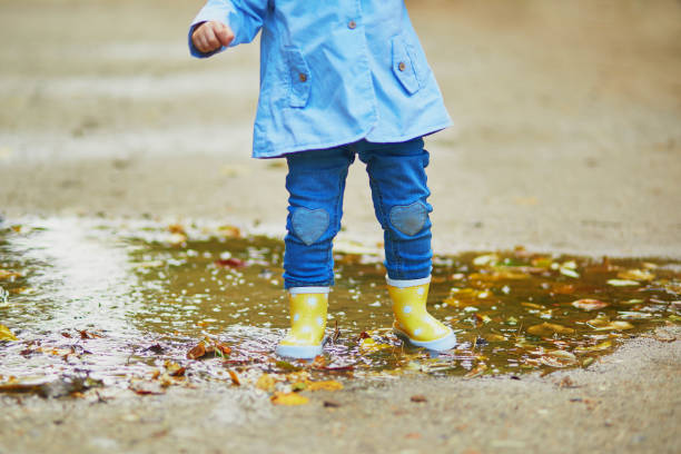 istock Child wearing yellow rain boots and jumping in puddle 1182846903