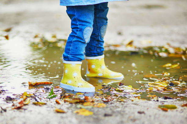 istock Child wearing yellow rain boots and jumping in puddle 1182846912