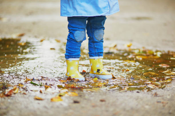 istock Child wearing yellow rain boots and jumping in puddle 1182846923