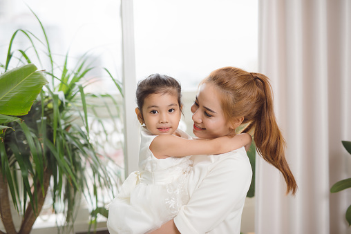 Happy asian mother hugging with her cute little daughter at home