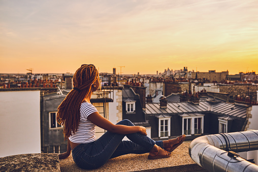 Full length shot of an attractive young woman sitting on a rooftop and looking at the cityscape in Paris, France