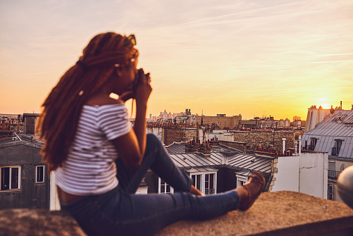 Shot of an attractive young woman sitting on a rooftop and taking pictures of the beautiful city of Paris, France