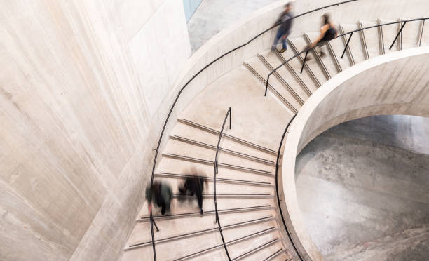 Blurred Motion of People on Spiral Staircase Color image depicting an abstract high angle view of a concrete spiral staircase. We can see the blurred motion of a group of people walking up and down the staircase, giving the impression that they are moving fast.  Room for copy space. ***image taken in City Hall, London, UK, a publicly owned building freely accessible to the public without entry fees or photographic restrictions*** staircase stock pictures, royalty-free photos & images