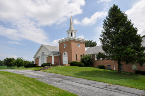 exterior of a red brick church in the country with a green grass lawn and blue sky with white clouds.  The church is in Bethlehem, Pennsylvania, United States.