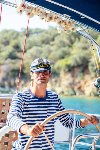 Handsome young man with captain cap on a sailboat at sea on a suuny day