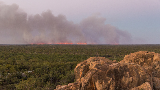 Bush or wild fire on the horizon in save distance from a high view point with rocks in foreground and bush trees. Shot close to Undara.