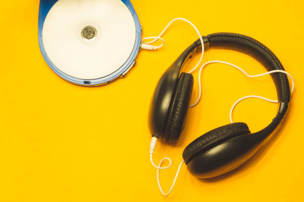 Headphones with a white cable on a yellow background. compact disc player with white cd and earphones Black headphones with a white cable on a yellow background. compact disc player with white cd and earphones cd player stock pictures, royalty-free photos & images