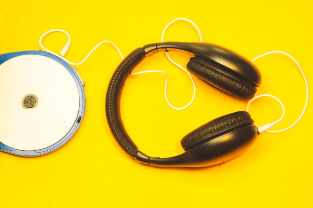 黄色の背景に白いケーブルが付着したヘッドフォン。白いcdとイヤホンを備えたコンパクトディスクプレーヤー - cd player ストックフォトと画像